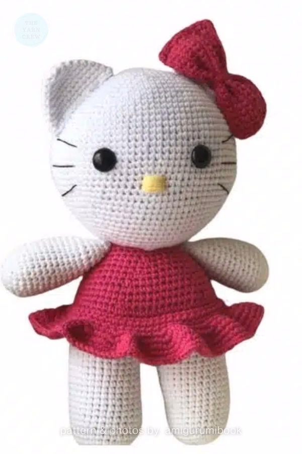 A crocheted Hello Kitty doll wearing a bright pink ruffled dress and a matching pink bow on her head, featured in a crochet roundup from https://theyarncrew.com/.