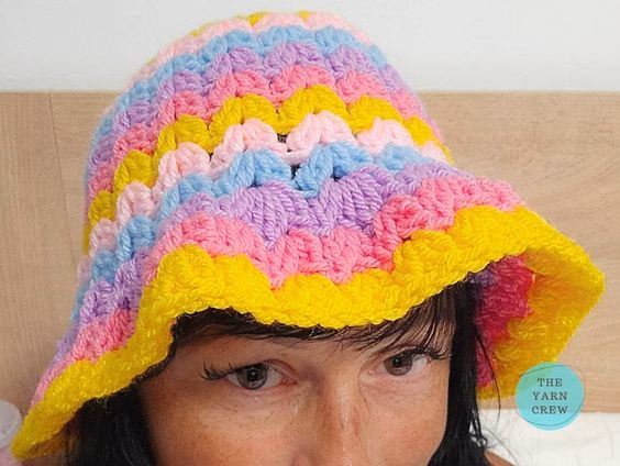 Colorful crochet bucket hat made with pink, yellow, blue, and purple yarn in a wavy stripe pattern. Original design created by Ariana Wimsett at TheYarnCrew.com.