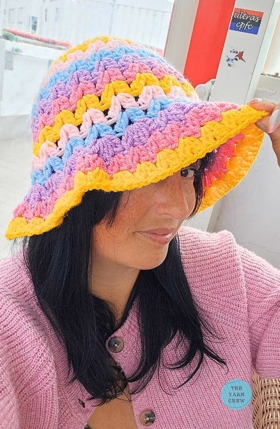 Colorful crochet bucket hat made with pink, yellow, blue, and purple yarn in a wavy stripe pattern. Original design created by Ariana Wimsett at TheYarnCrew.com.