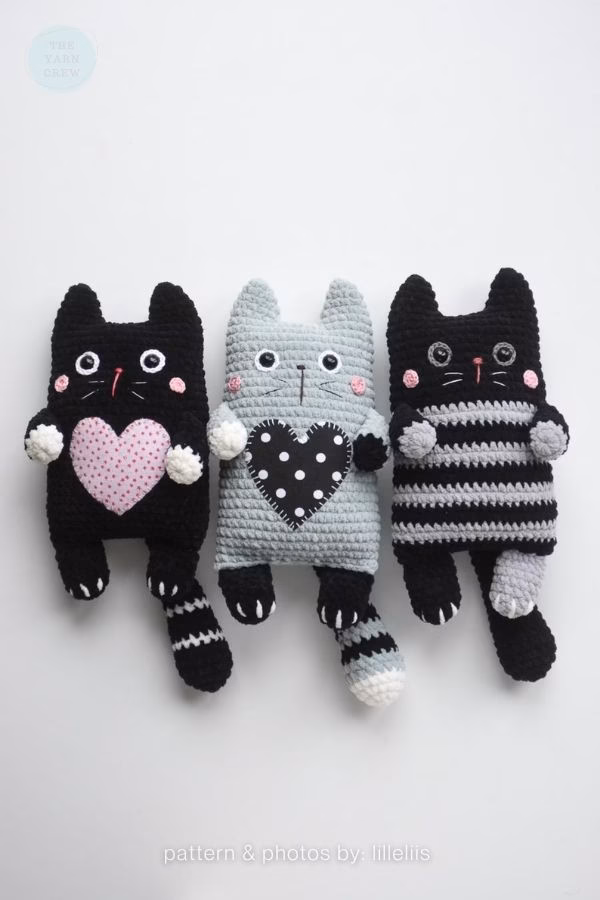 Three flat-style crochet cats in black and gray, featuring decorative hearts or stripes; from a roundup on TheYarnCrew by Ariana Wimsett.