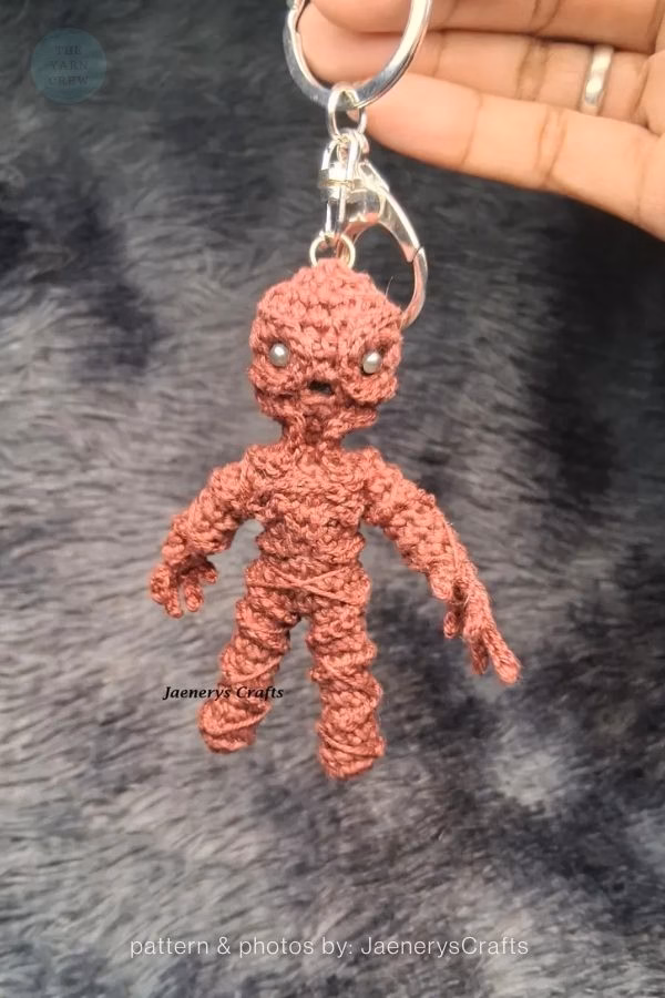 A hand holding a small, brown crochet keychain of the Vecna monster from Stranger Things. Curated by Ariana of TheYarnCrew.