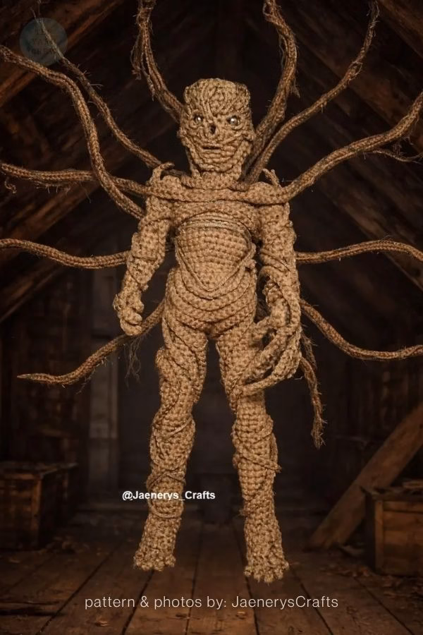 A highly detailed brown crochet doll of Vecna from Stranger Things with long yarn tentacles spreading out behind him. Curated by Ariana of TheYarnCrew.