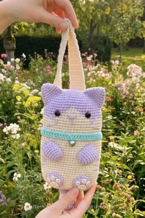 A tall crochet cat pouch in light purple and cream with a teal collar and carrying strap; from a roundup on TheYarnCrew by Ariana Wimsett.