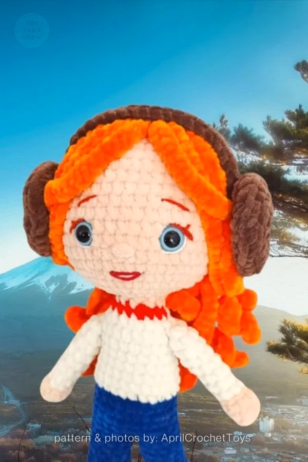 A soft, fluffy crochet doll of Max from Stranger Things with bright orange yarn hair and brown winter earmuffs. Curated by Ariana of TheYarnCrew.