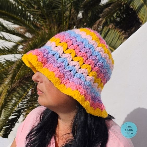 Colorful crochet bucket hat made with pink, yellow, blue, and purple yarn in a wavy stripe pattern. Original design created by Ariana Wimsett at TheYarnCrew.com.
