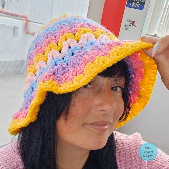 Colorful crochet bucket hat made with pink, yellow, blue, and purple yarn in a shell stitch wave pattern. Original design created by Ariana Wimsett at TheYarnCrew.com.
